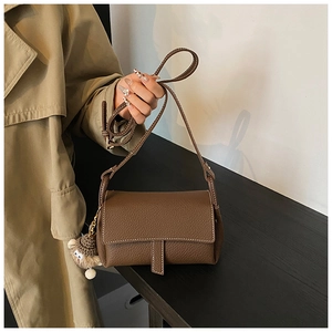Gros plan du sac bandoulière en cuir marron foncé avec un porte-clé en peluche