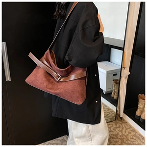 Détail d'un sac cabas rétro en daim marron avec large bandoulière porté par un modèle