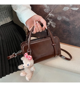 Detail of dark brown leather Boston bag with brand logo and cute plush bear charm