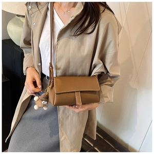Sac bandoulière en cuir marron avec coutures blanches et peluche sur un trench beige