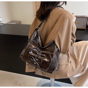 Close-up of brown polished leather shoulder bag with chic bow pleats and slim straps