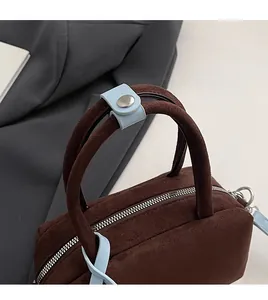 Detail of brown suede handbag featuring blue leather strap accent and silver metal zipper