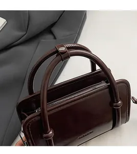 Detail of dark brown leather handbag featuring sleek cylindrical handle and metal hardware