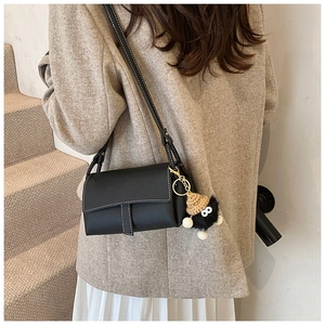 Détail du sac bandoulière en cuir grainé noir avec surpiqûres blanches et charme peluche