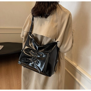 Detailed view of black patent leather tote bag with large bow and white topstitching