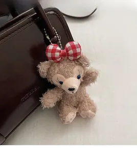 Close-up of a plush ShellieMay charm with a red checkered bow on a brown leather bag