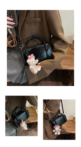 Detail of black glossy Boston bag with plush bear charm and brand embossed texture