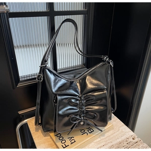 Detail of black glossy leather shoulder bag with white contrast stitching and bow decoration