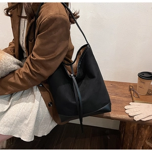 Detail of a black canvas bucket bag with leather base held by a model on a wooden bench