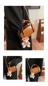 Detail of a brown faux leather handbag featuring a plush bear charm and crossbody strap