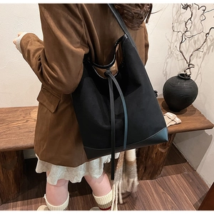 Detail of a large black suede tote bag with leather straps and drawstring knot accents