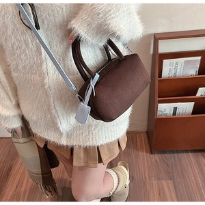 Detail of a dark brown suede handbag with light blue shoulder strap and contrast tag