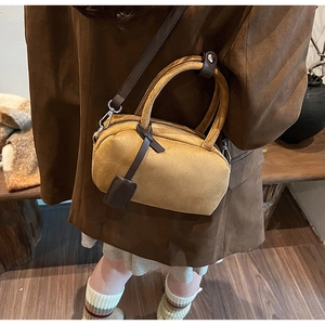 Close-up of a frosted suede top handle bag in camel brown with a minimalist leather tag