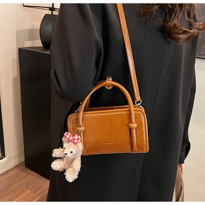 Detail of a brown leather Boston bag with a plush bear charm on a female model