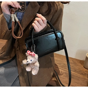 Close-up of black glossy leather handbag with teddy bear charm on wood background