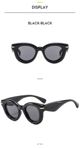 Detail view of black cat-eye sunglasses with golden streamline metal accents and thick frames