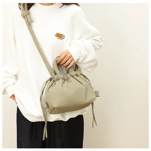 Model wearing an olive green quilted crossbody bag with drawstring closure and soft handles