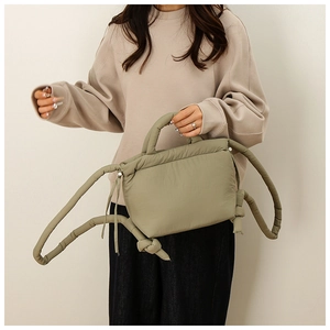 Detail of sage green puffer bag showing thick tubular handles and knotted strap design