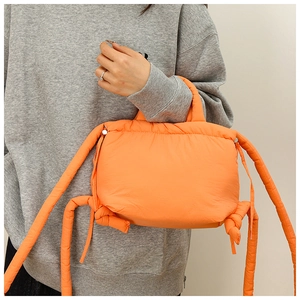 Detail of bright orange puffer nylon bag with soft tubular straps and stylish knot accents