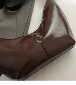 Close-up of glossy brown faux leather material with fine stitching on a shoulder bag