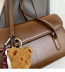 Detail of a brown leather shoulder bag featuring a cute bear charm and woven rope accent