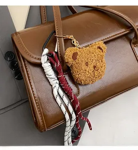 Detail of plush bear charm with golden chain and woven cord on brown leather tote bag