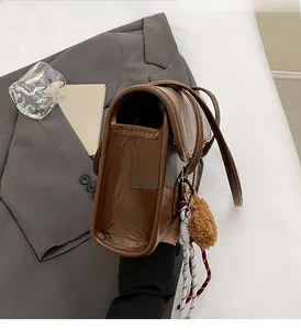 Detail of dark brown vintage shoulder bag with plush charm on gray blazer background