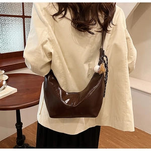 Detail view of large dark brown crescent bag with baseball charms on leather shoulder strap