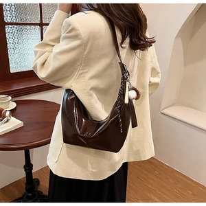 Detail of a coffee brown faux leather half-moon bag with a unique baseball bat pendant