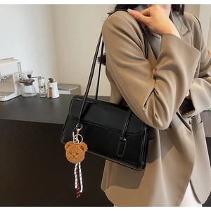 Detail of black leather shoulder bag with plush bear charm worn with khaki blazer