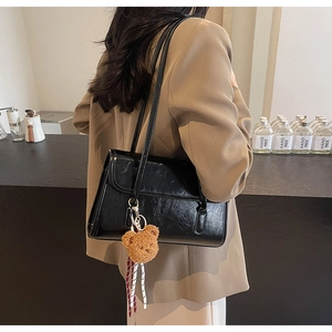 Detail of glossy black underarm bag with a cute bear charm, side view on shoulder