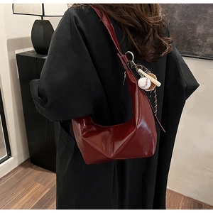Detail showing high-gloss burgundy crescent shoulder bag with creative baseball charm