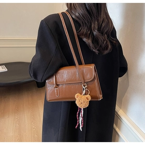 Detail view of retro brown shoulder bag with a cute plush bear charm and ribbon