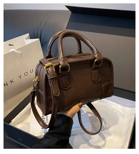 Detailed close-up of dark brown leather pillow bag with gold hardware and gift packaging