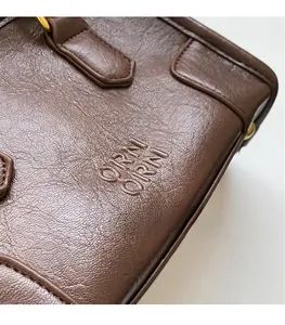 Close-up of textured dark brown leather pillow bag with gold hardware and logo
