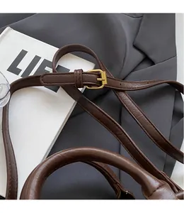 Detail of adjustable slim brown leather shoulder strap with a golden square buckle