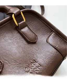 Detail of dark brown lychee leather handbag featuring gold metal rings and embossed logo