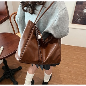 Detail of vintage brown leather tote bag featuring a baseball charm and woven strap