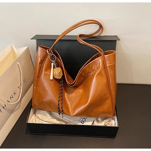 Detail of a brown leather tote bag with a decorative pendant in a premium gift box