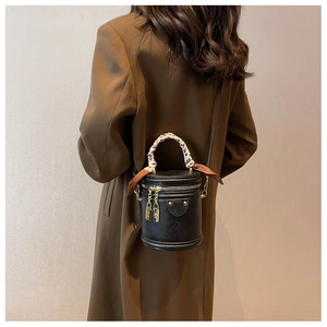 Détail d'un sac seau noir avec anse foulard léopard et détails dorés porté par un mannequin
