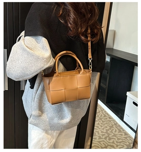 Detail of woven caramel crossbody bag with structured double handles and slim strap
