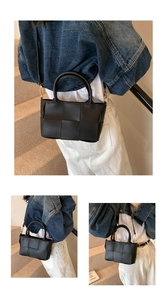 Detail of black woven crossbody bag with dual handles and gold hardware on stairs