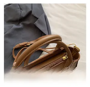 Detail of brown PU leather handbag featuring metal zipper and sturdy round handles