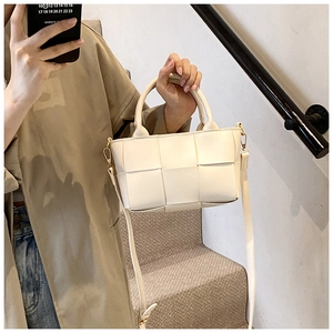 Close-up of beige woven crossbody bag with dual handles and gold hardware details