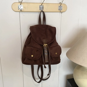 Vintage dunkelbrauner Wildlederrucksack mit Fronttaschen an weißem Wandhaken aus Holz