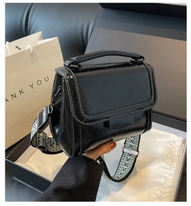 Detail of glossy black leather crossbody bag with white stitching in a gift box packaging