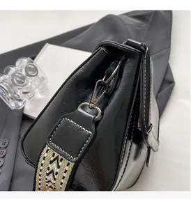 Nahaufnahme der schwarzen glänzenden Tasche mit weißen Kontrastnähten und Web-Schultergurt