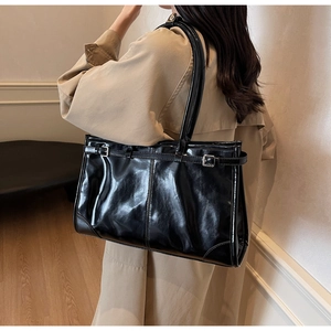 Detail shot of a black glossy tote bag with metal buckles on a model in a trench coat