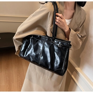 Detail of glossy black patent leather shoulder bag with buckle strap on a trench coat