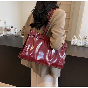 Detail of a large burgundy glossy tote bag shown from a side view on a female model